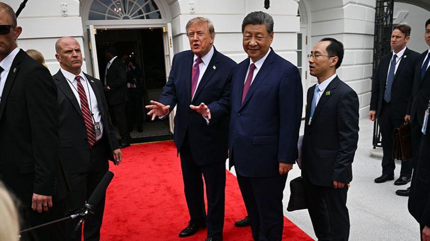 Trump gestures while standing next to Xi on a red carpet, surrounded by staff