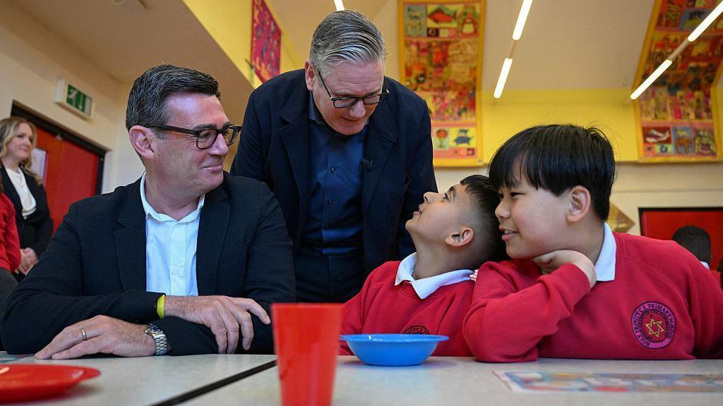 Sir Keir Starmer looks over the shoulder of Andy Burnham as they chat to two children in school uniform on a visit to a breakfast club in Ashton-under-Lyne, Greater Manchester, in April.