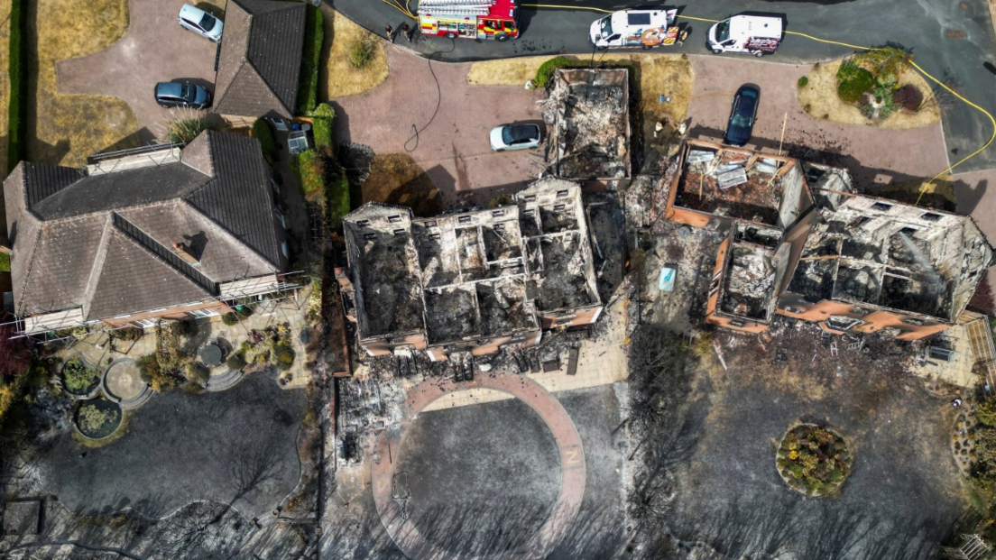 The remains of three homes destroyed by the wildfires, with charred gardens and near a railway line.