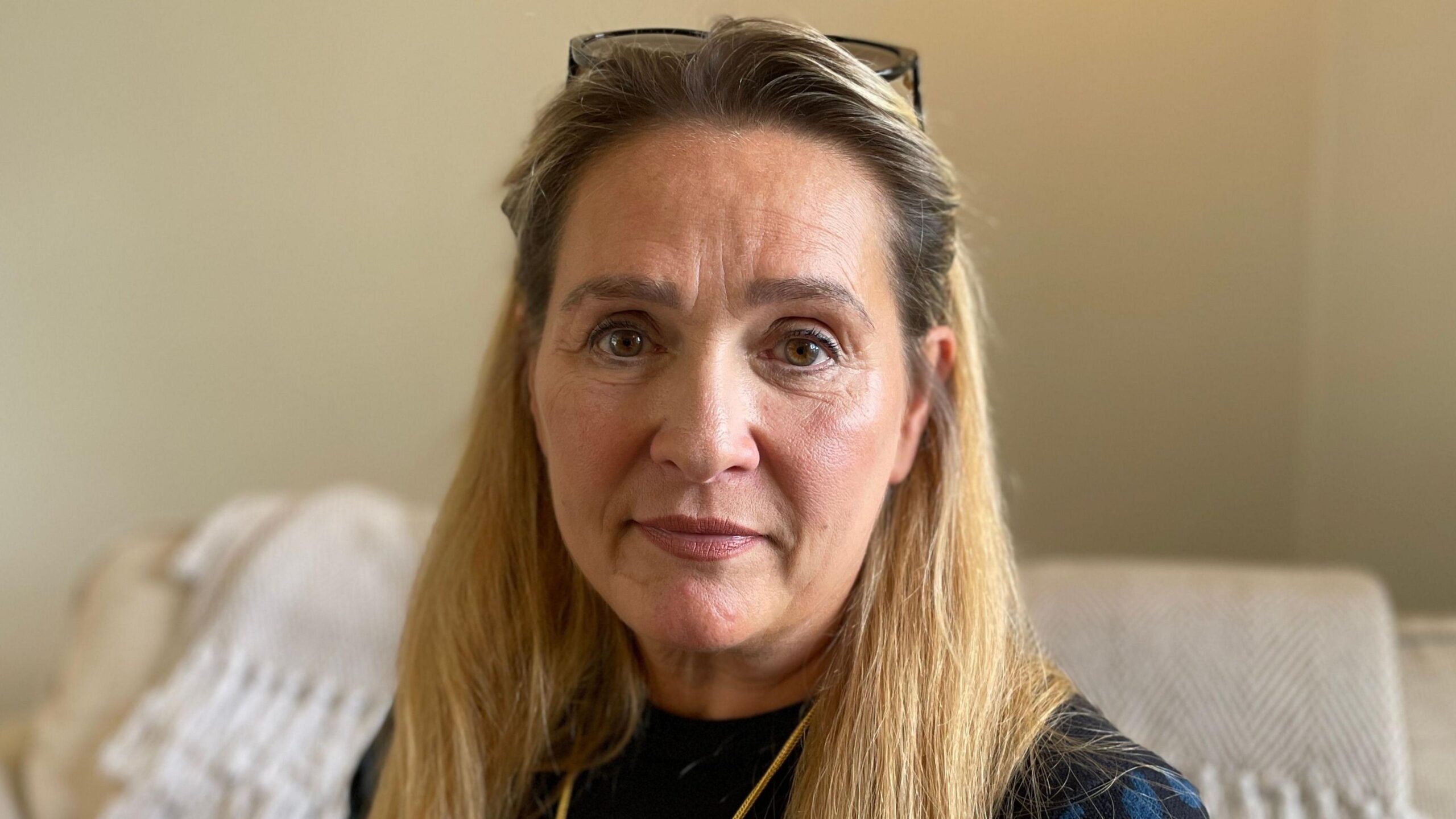 A head and shoulders image of a woman who is looking directly into the camera. She has glasses resting on the top of her head.