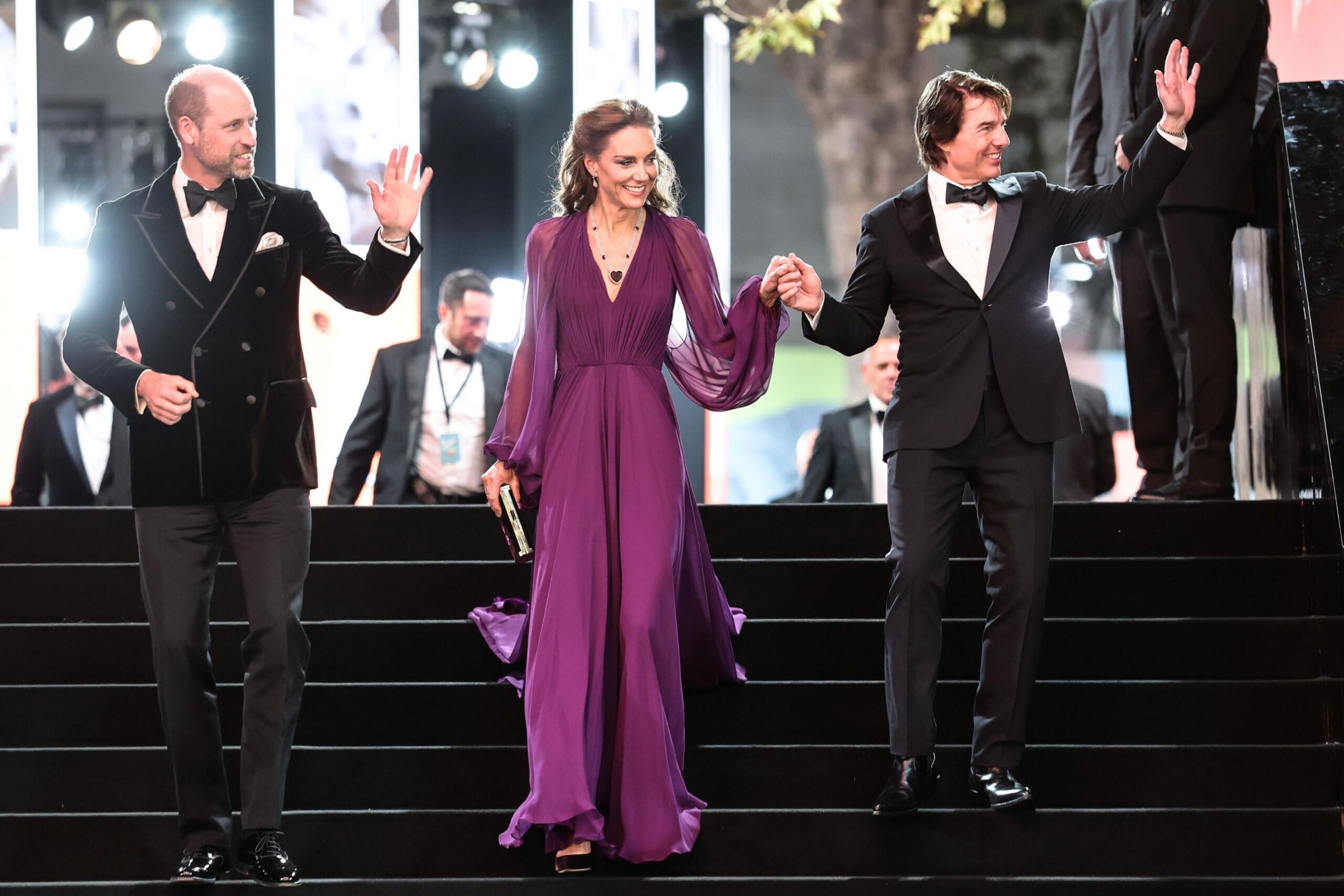 The Prince and Princess of Wales with Tom Cruise walking down stairs together with a black carpet, with Cruise holding the Princess of Wales's hand