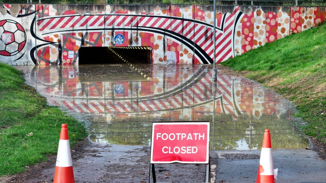 A flooded footpath leading to an underpath with warning cones and a 