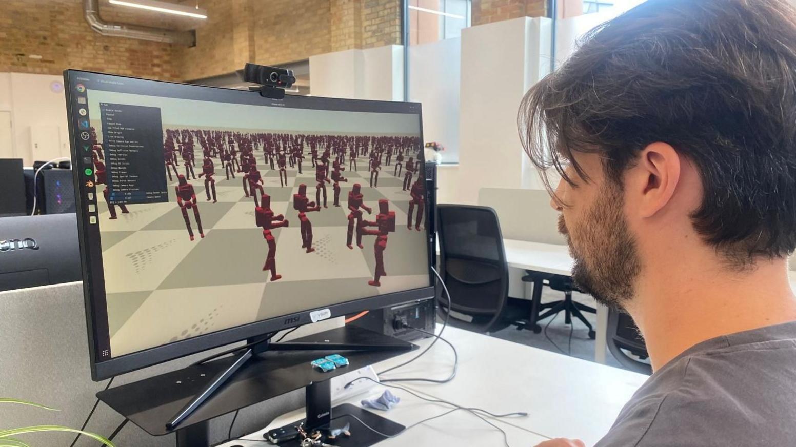A Vsim worker sits at a computer looking at a screen which has multiple robots moving on a grid.