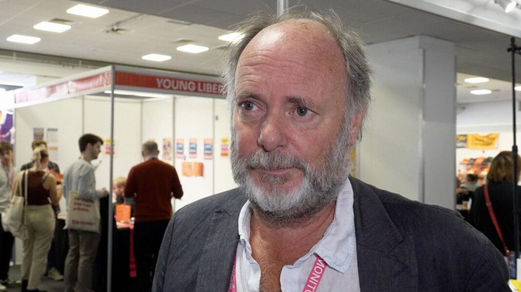 Julian Brazil, a bearded man in an open necked shirt and Lib Dem lanyard, speaks to the BBC in the exhibition hall at the Lib Dem conference