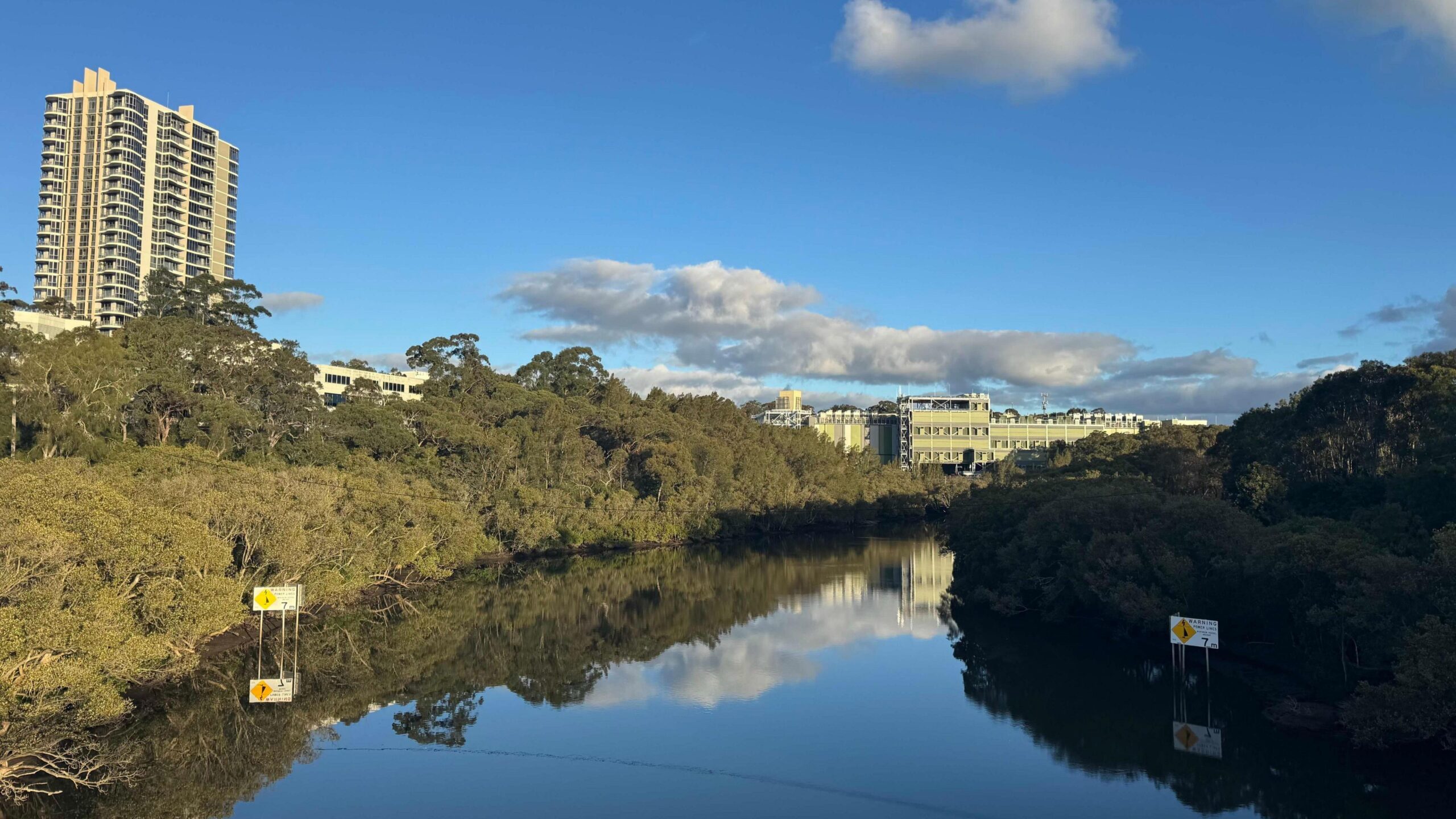 A view of the river, lined with dense green trees on both banks - and the Lane Cove data centre in the background