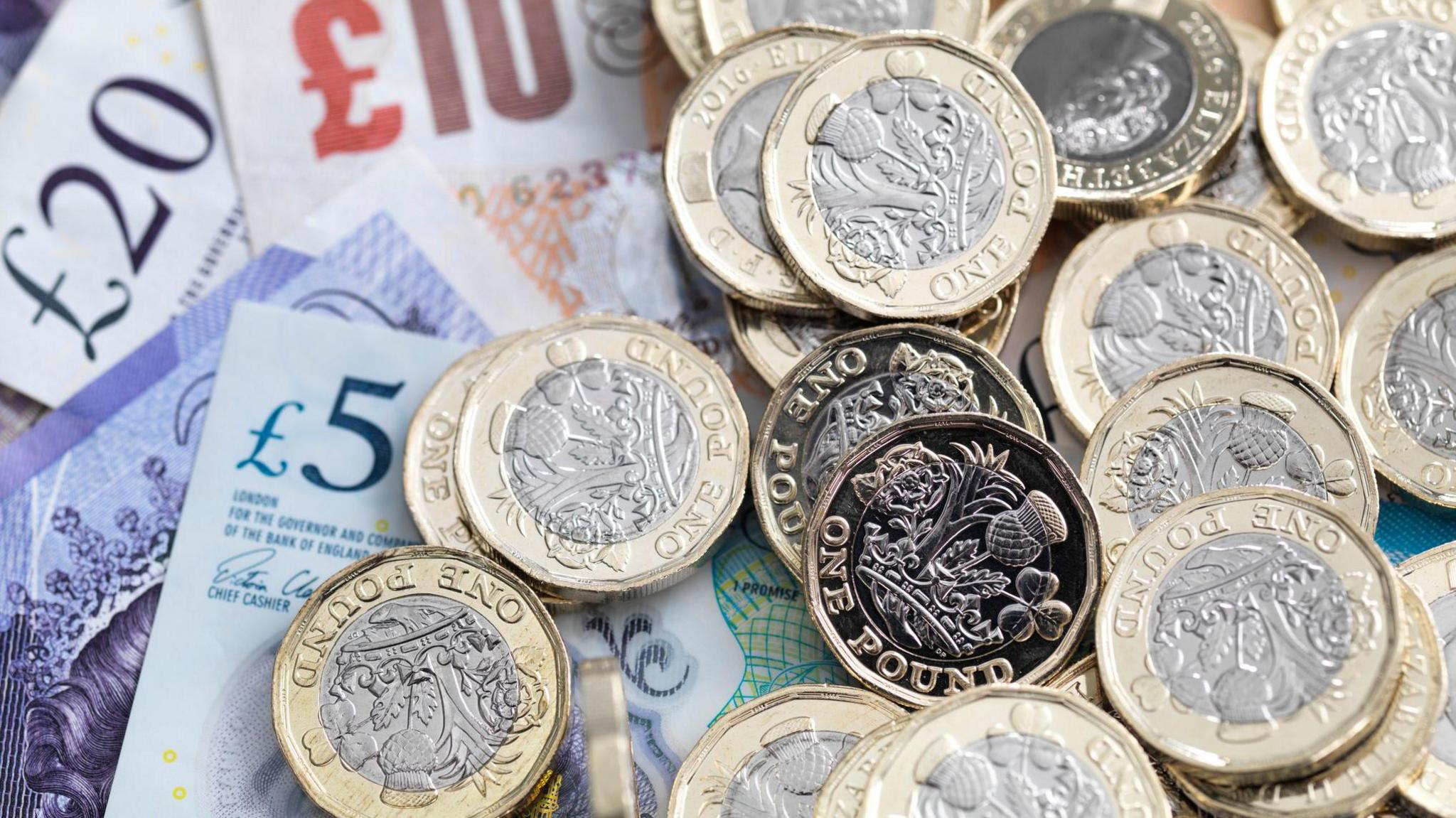 Pound coins piled on top of bank notes including £5, £10 and £20.