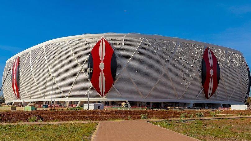 Exterior of a football stadium showing three Kenyan shields in red, white and black on top of a white wrap around