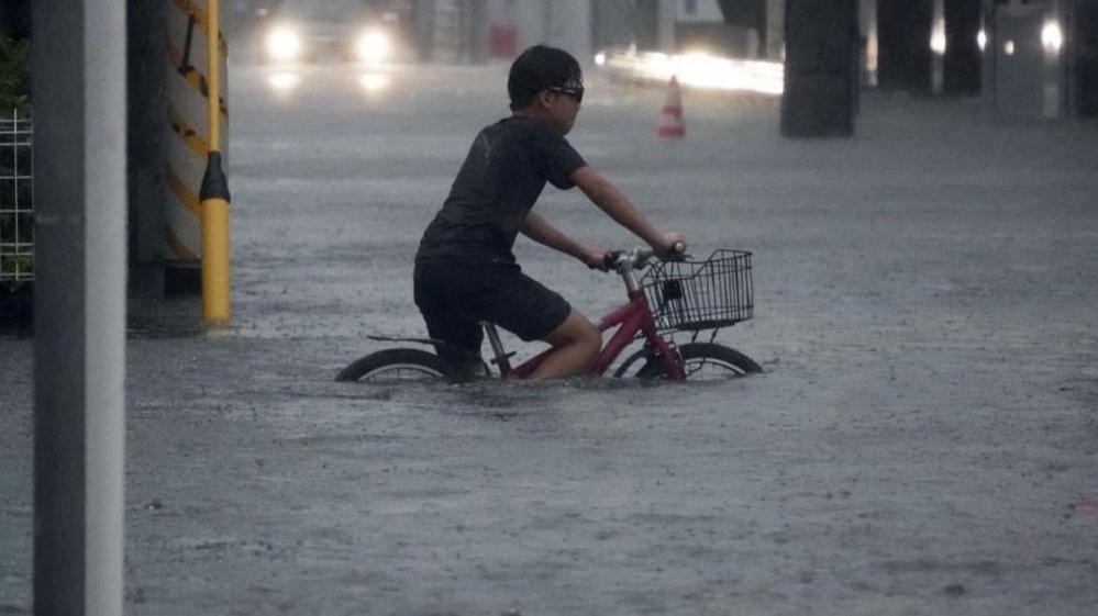 A man rides a bike almost completely submerged in rain water.