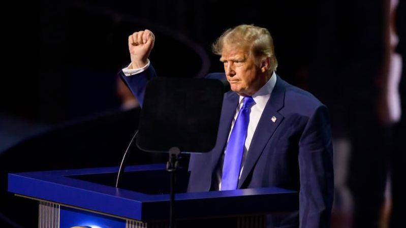 Trump wearing a blue suit and tie and white shirt opens his arms as he addresses the convention in Dallas