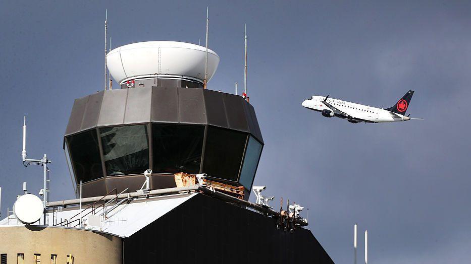 An air traffic controller tower in Boston, seen in 2025, with an Air Canada plane taking off in the background