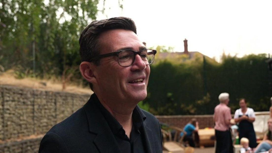 Andy Burnham, who wears a dark coloured suit, smiles from an outdoor area at a family centre in Sheffield.