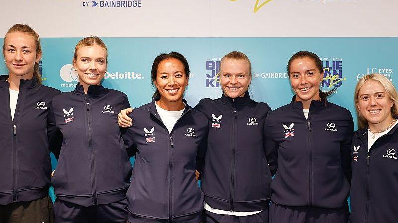 Mika Stojsavljevic, Katie Boulter, Anne Keothavong, Harriet Dart, Jodie Burrage and Sonay Kartal pose for a photograph with arms around each other, all wearing zip-up blue team tracksuit tops