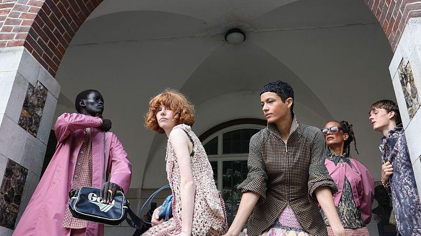 Models backstage during London Fashion Week in September 2026 . There are five models waiting under an arch, wearing an assortment of outfits with a pink and checkered theme.