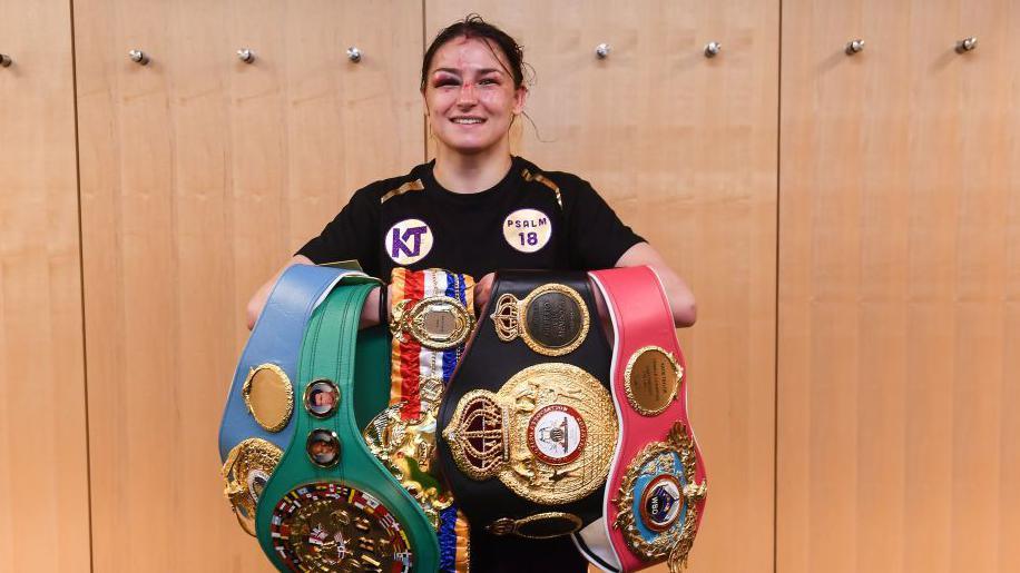 A bruised Katie Taylor grins with all her belts
