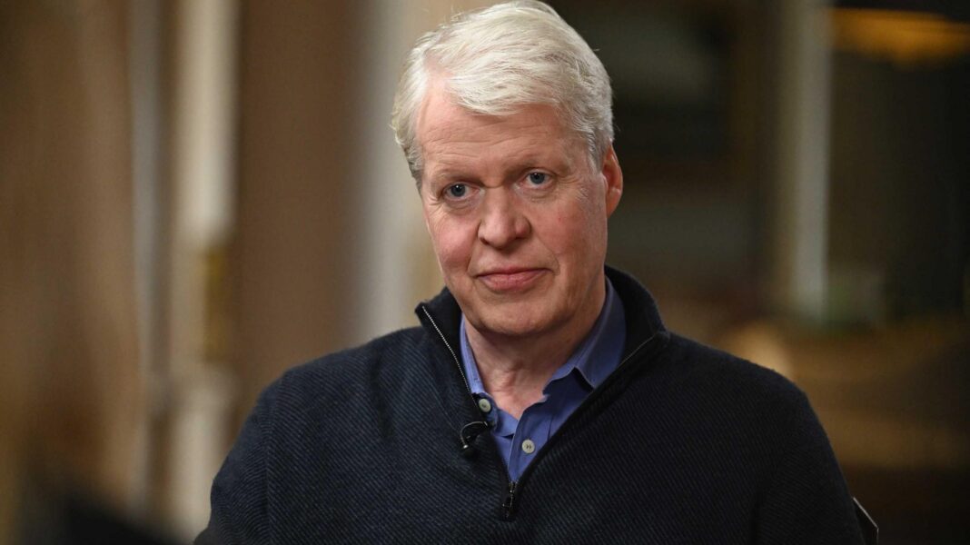 Earl Spencer sitting on a chair in a black three quarter-zip sweater and blue shirt. He sits in a room at the Althorp estate.