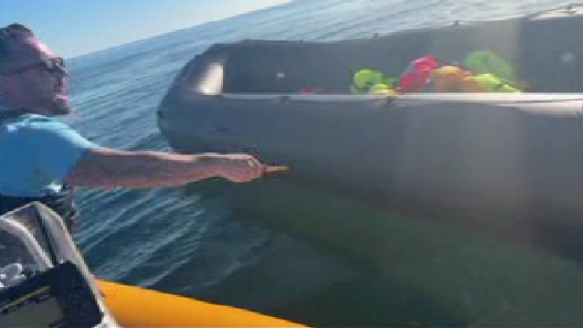 Anti-migrant campaigner leaning out of a boat appearing to hold a knife and to be shouting