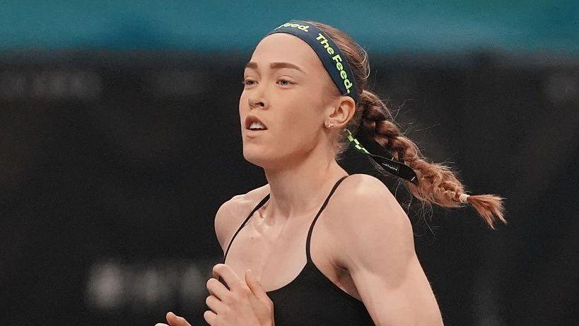 Joanna Wietrzyk wears a black sports bra and a dark headband with the words 'the feed' printed in green letters. Her hair is tied back into a plait and she is mid-run.