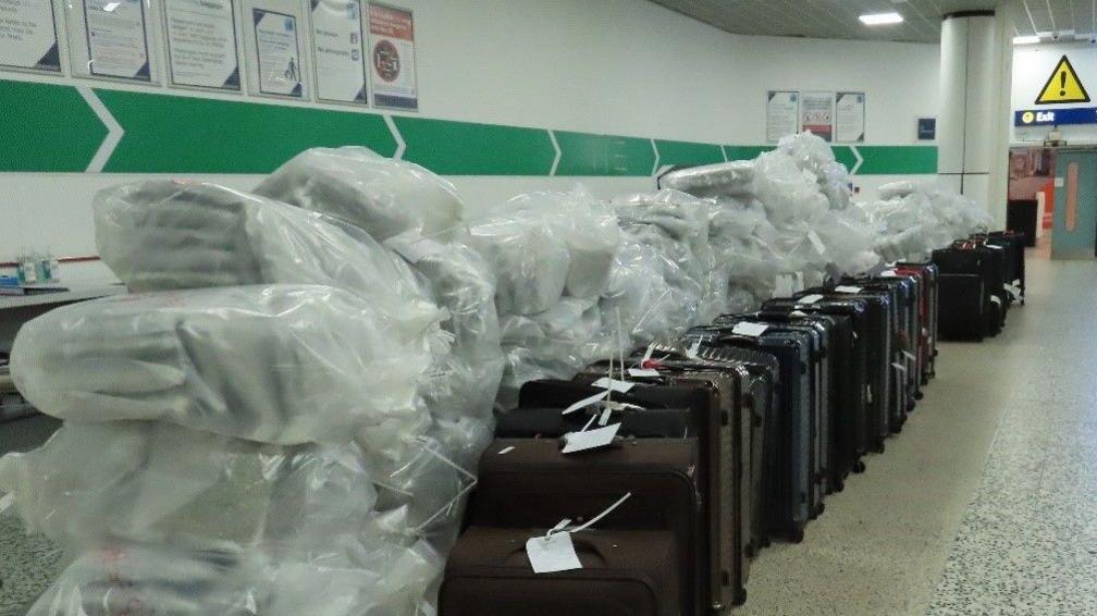 Large bags of cannabis next to a row of suitcases in an airport