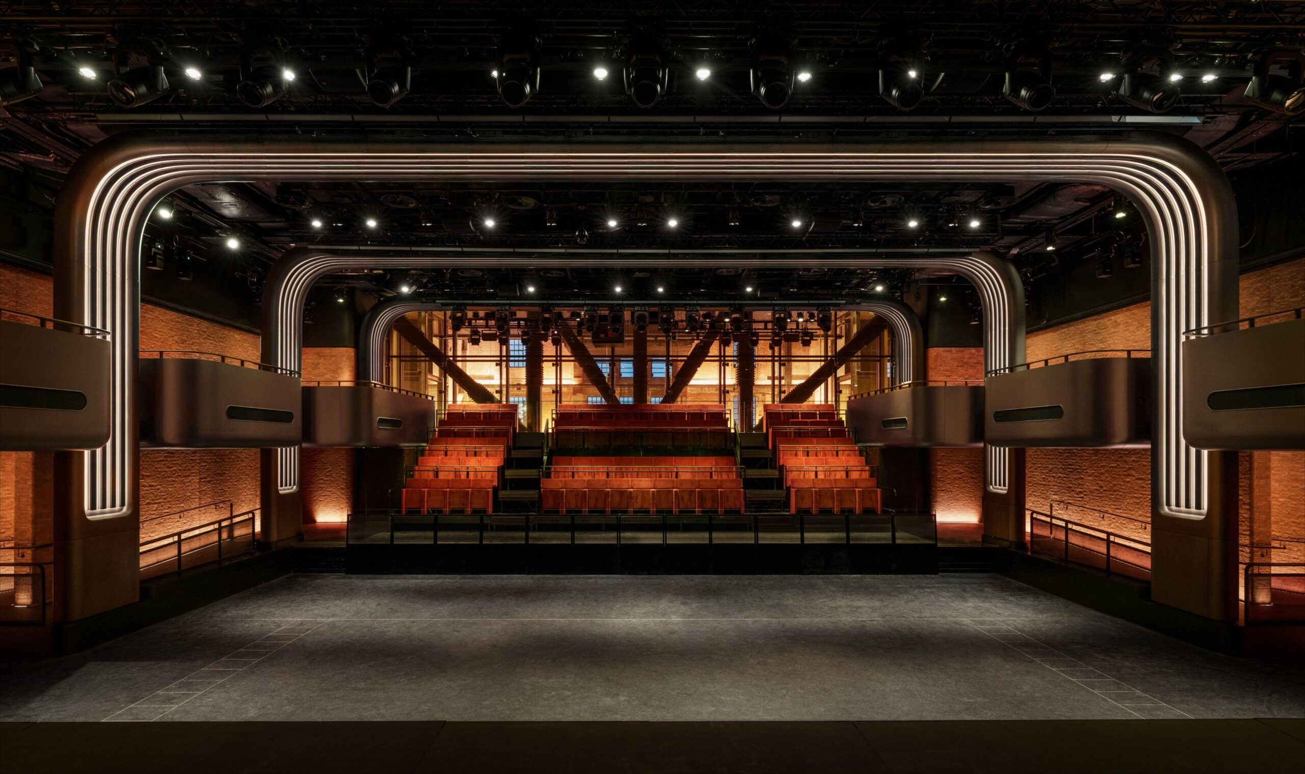 Inside Apple Music's new music venue in London. The photo shows tiered seating and staggered boxes for an elevated view of the stage. The back wall is made of glass and offers views of an entry lobby and the Thames