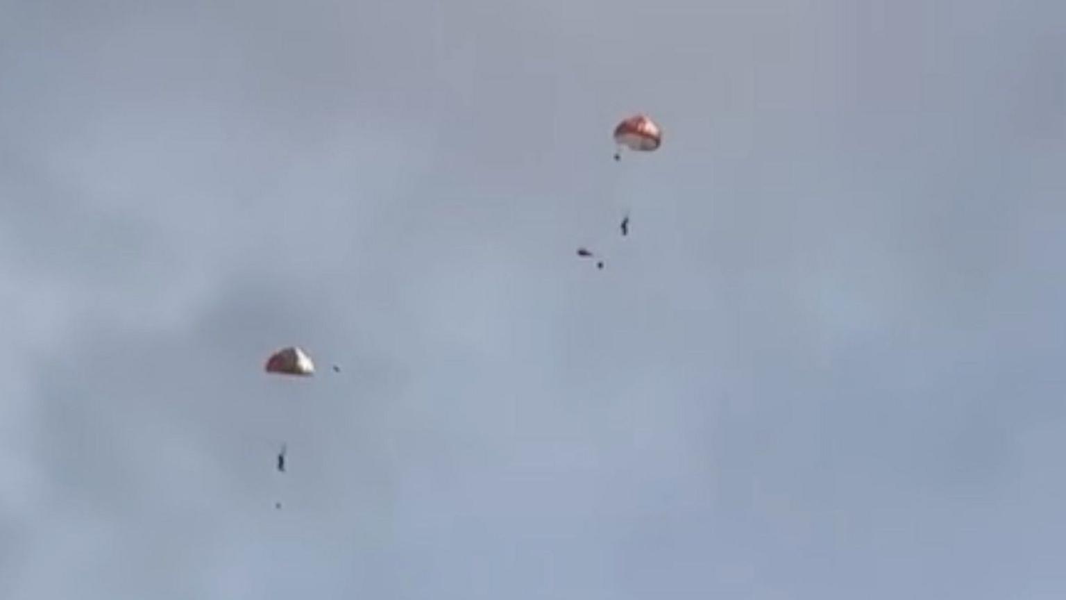 Two figures floating in the sky with parachutes