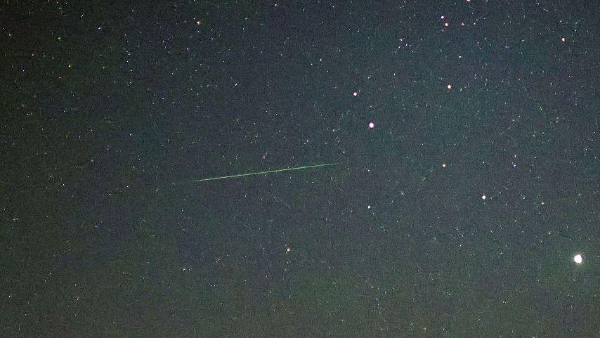 A green line cuts through a starry sky, capturing a meteor passing through the atmosphere.