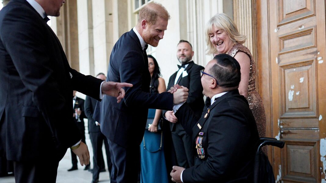 Charles ‘sounded giddily elated’ after Diana died, Earl Spencer claims Prince Harry, Duke of Sussex, shakes hands with a man in a wheel chair dressed in a black suit bedazzled with war medals at the inaugural Invictus Spirit Awards