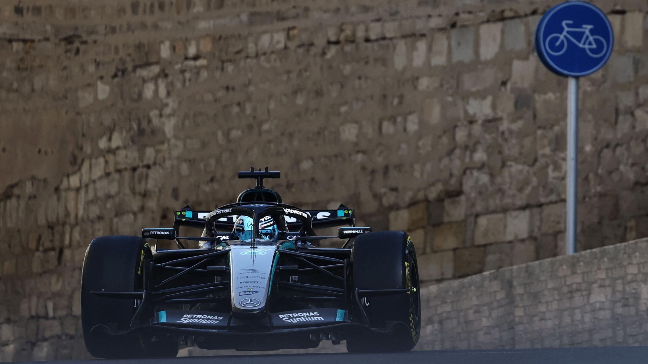 Mercedes' George Russell crests a hill during Azerbaijan Grand Prix second practice. In the background can be seen the walls of a castle and a cycling road sign