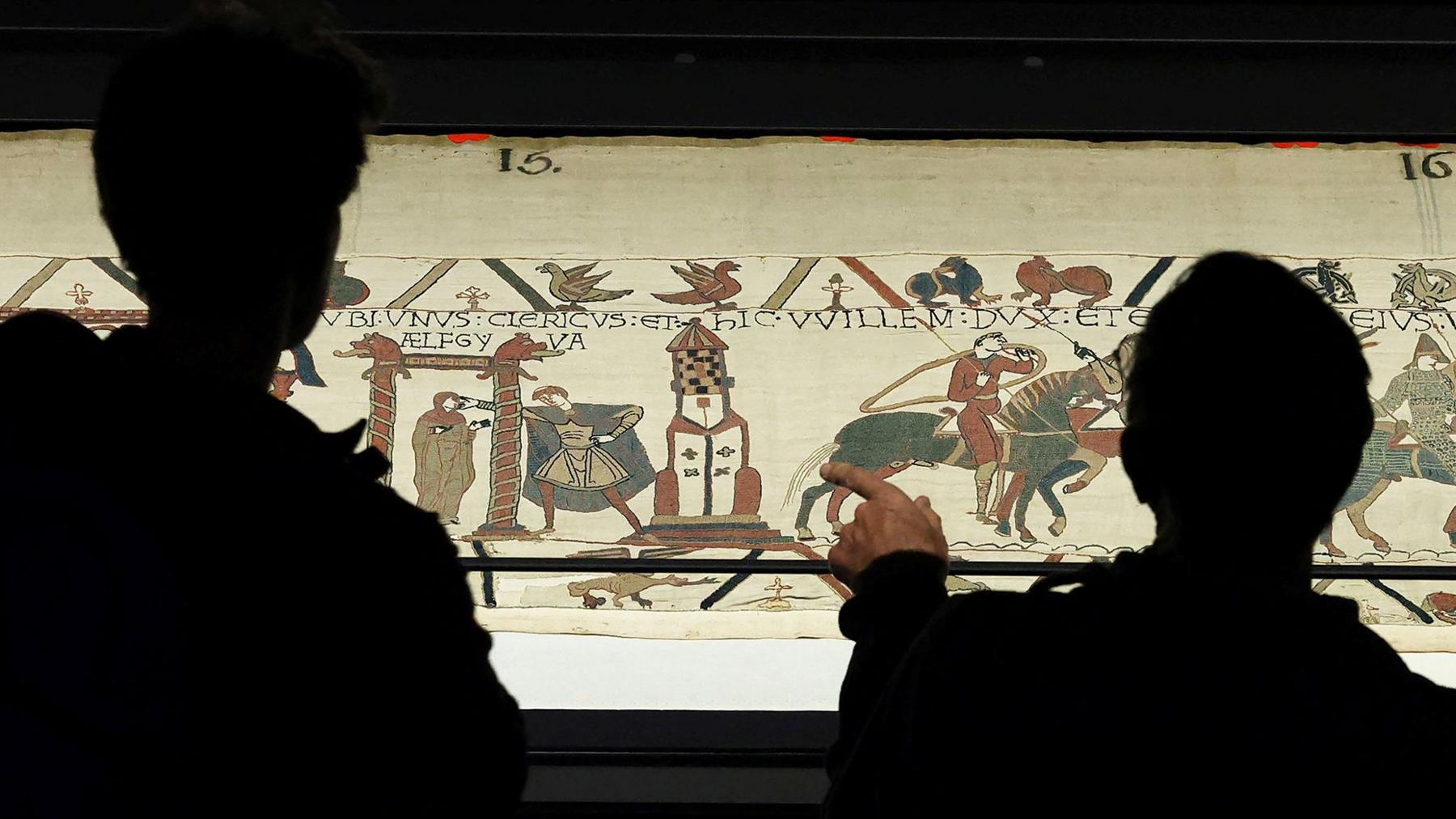 Shadowy figures of people viewing the Bayeux Tapestry up close