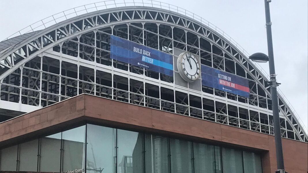 The exterior of Manchester Central. It has a steel arch and is draped with a banner from the Conservative party conference, which reads 'build back better' and 'getting on with the job'.