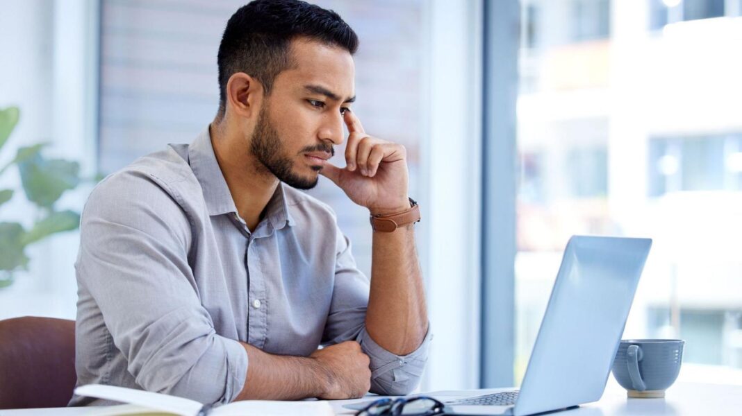 ‘I lost my savings after a job interview scam’ A man in a pale shirt sits at a laptop in an office