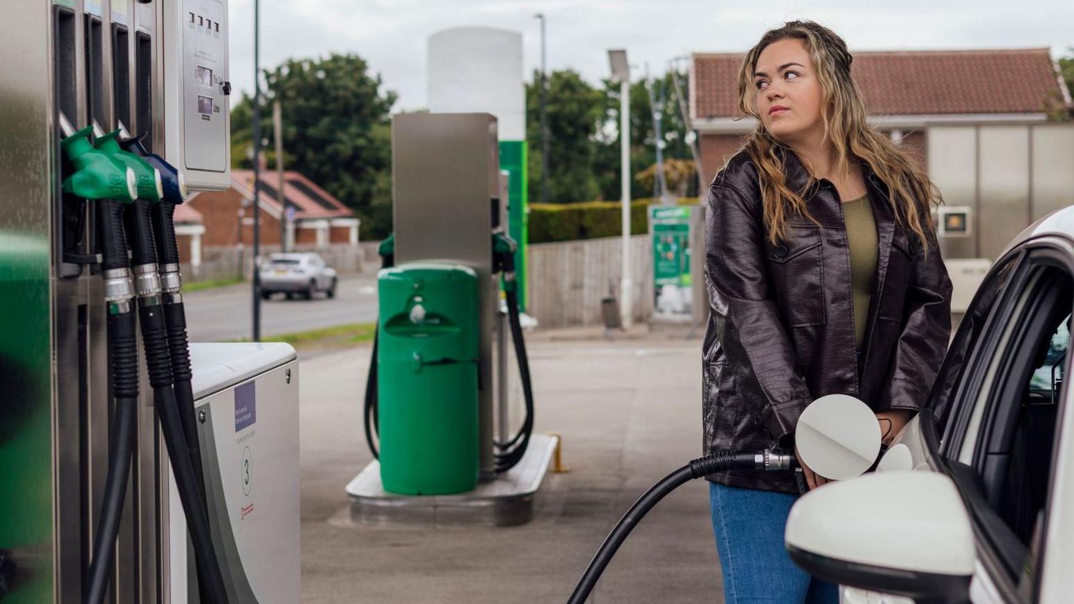 Woman filling her car at a petrol station in the North East of England. The woman is looking worriedly at the price on the screen