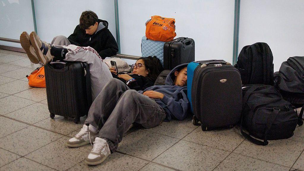 Young people lying on the floor of Gatwick Airport with their suitcases