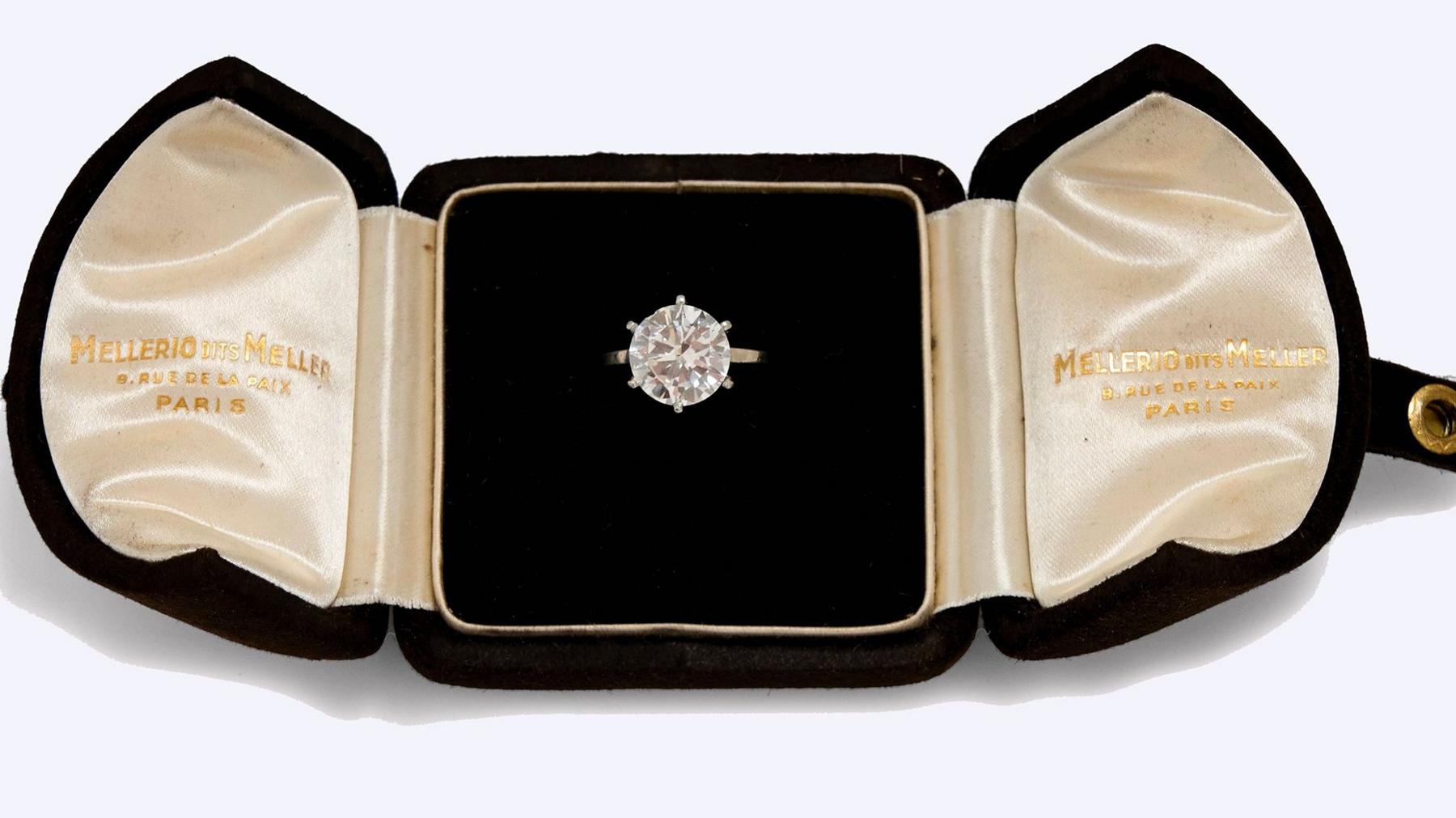 A large round diamond ring is seen displayed in an open black velvet ring case