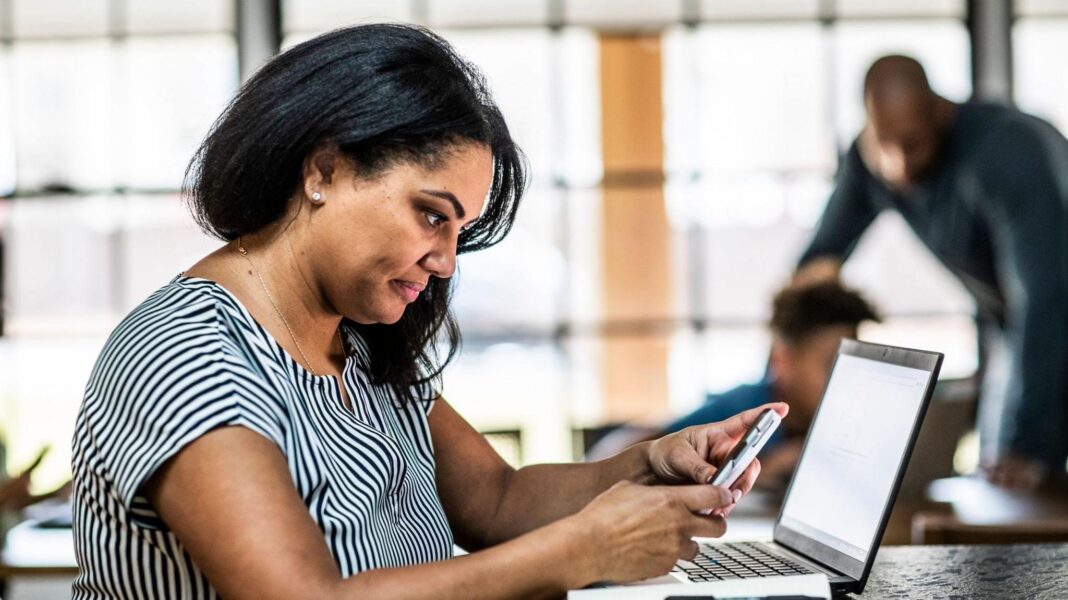 Will you get £13,000 a year when you stop working? Here’s how to check Woman looking at a phone sits at a desk with a laptop in front of her and a man and boy in the background.
