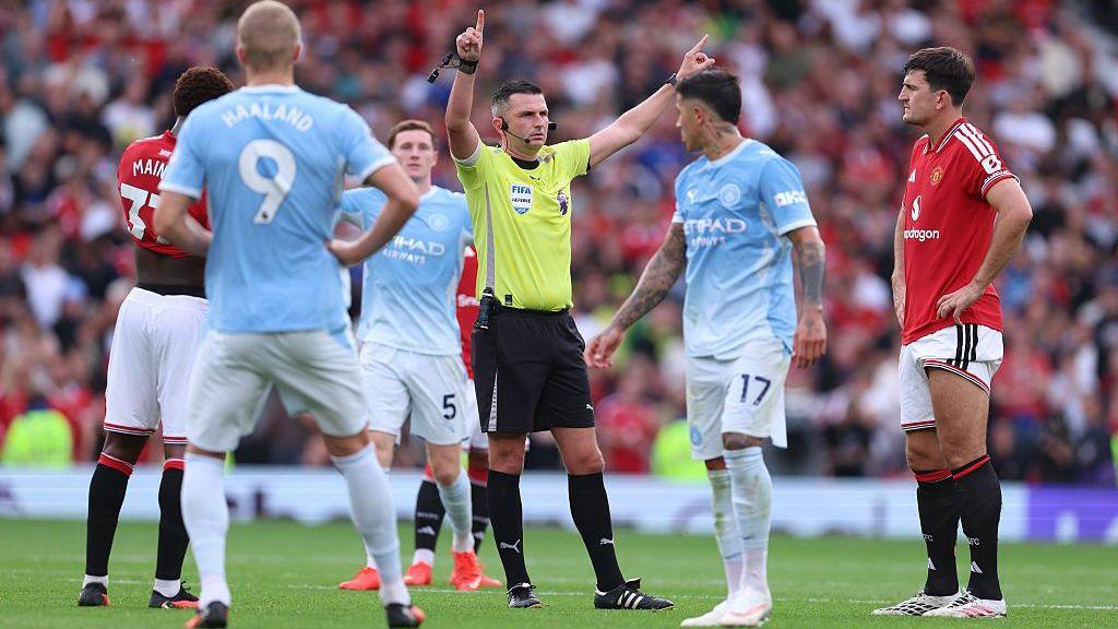 Players wait for referee Michael Oliver to reveal the VAR decision for the goal scored by Erling Haaland for Manchester City against Manchester United