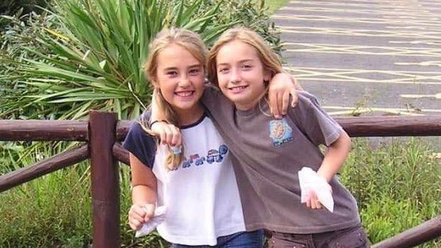 Maddy Cusack with her cousin Emily Reilly as children. Aged about 10, Maddy has her arm around her cousin as they both smile at the camera. They are pictured outside, holding small paper bags of sweets.