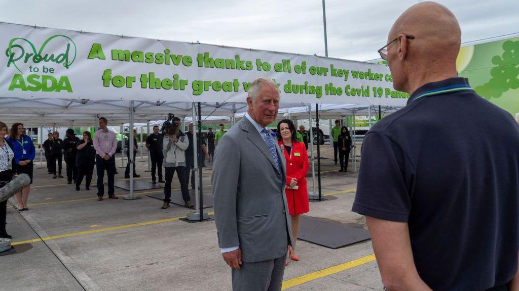 Trump shares misleading video of King and fainting worker Then-Prince Charles in a grey suit speaks to a man with his back to the camera who is wearing Asda uniform
