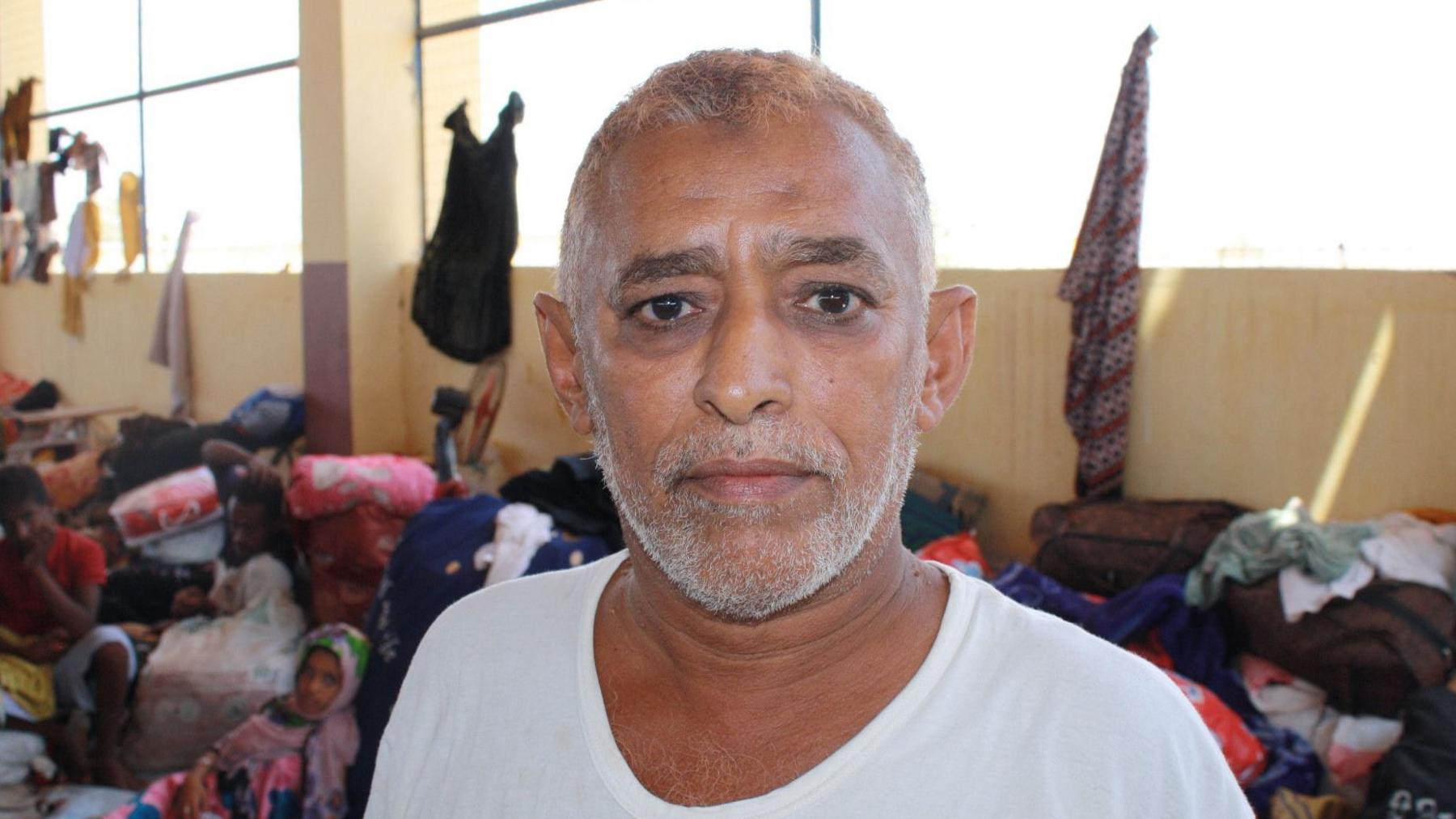 A man in a white t-shirt stands inside a refugee centre
