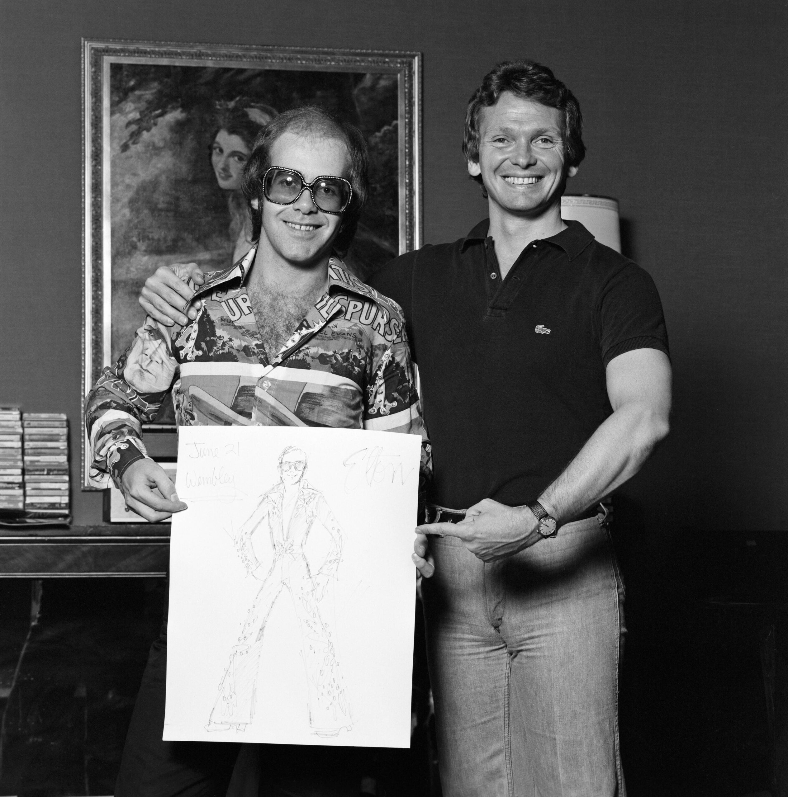 Bob Mackie stands next to Elton John, pointing at a sketch of the bejewelled baseball uniform he designed in 1975.