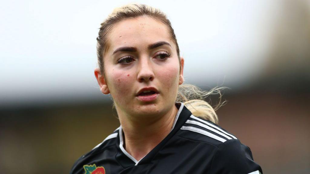 Maddy Cusack is seen during a match in this zoomed-in shot. She wears Sheffield United's black away kit, her blonde hair tied back in a pony tail. She is looking off to her side during what appears to be a break in the action.