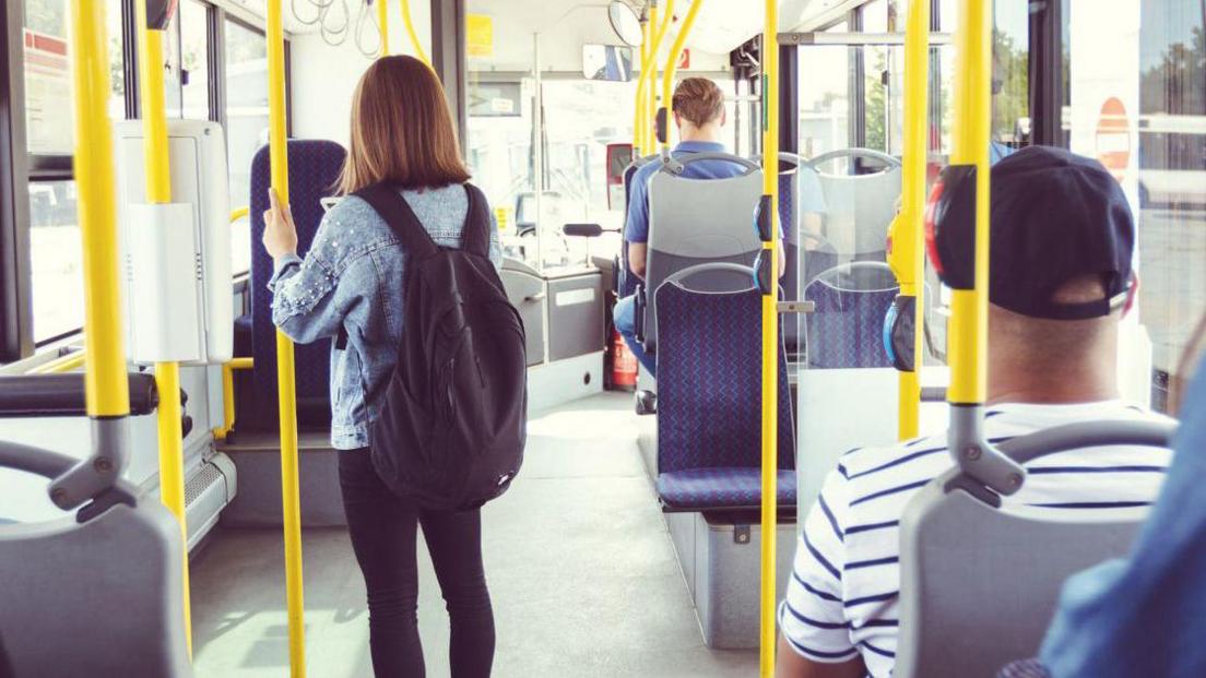 Males and females commuting by public transport - stock photo Men and women traveling in public transport. Teenage girl is standing at aisle while commuting by bus. They are in vehicle.