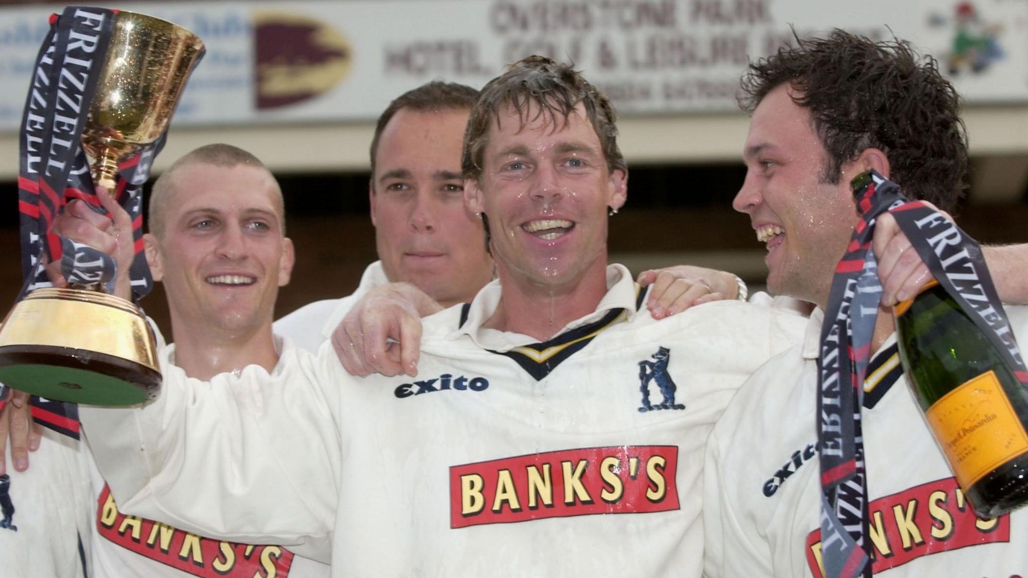 Nick Knight holds the 2004 Frizzell County Championship trophy in his right hand and holds a bottle of champagne in his left. He has three team-mates around him