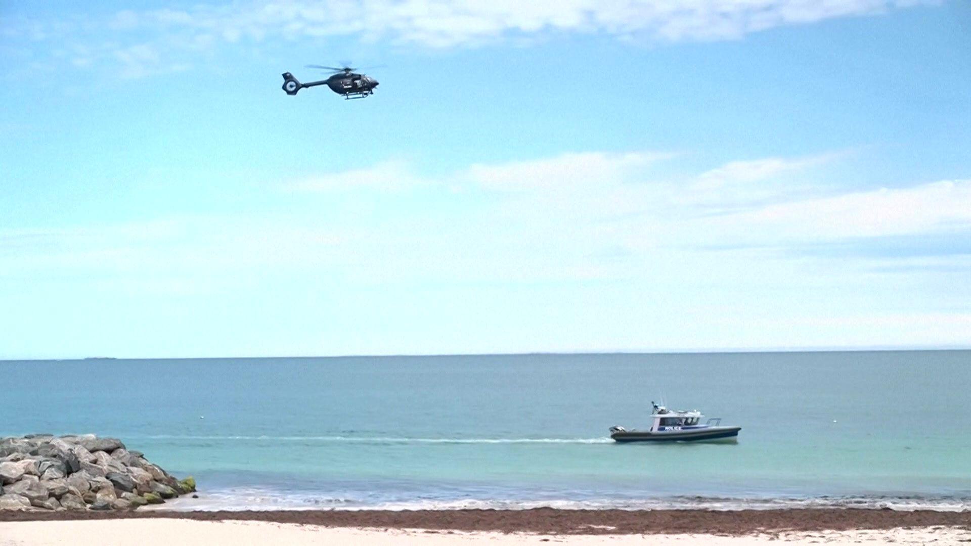 A police boat in the water and a helicopter in the air, flying over it.
