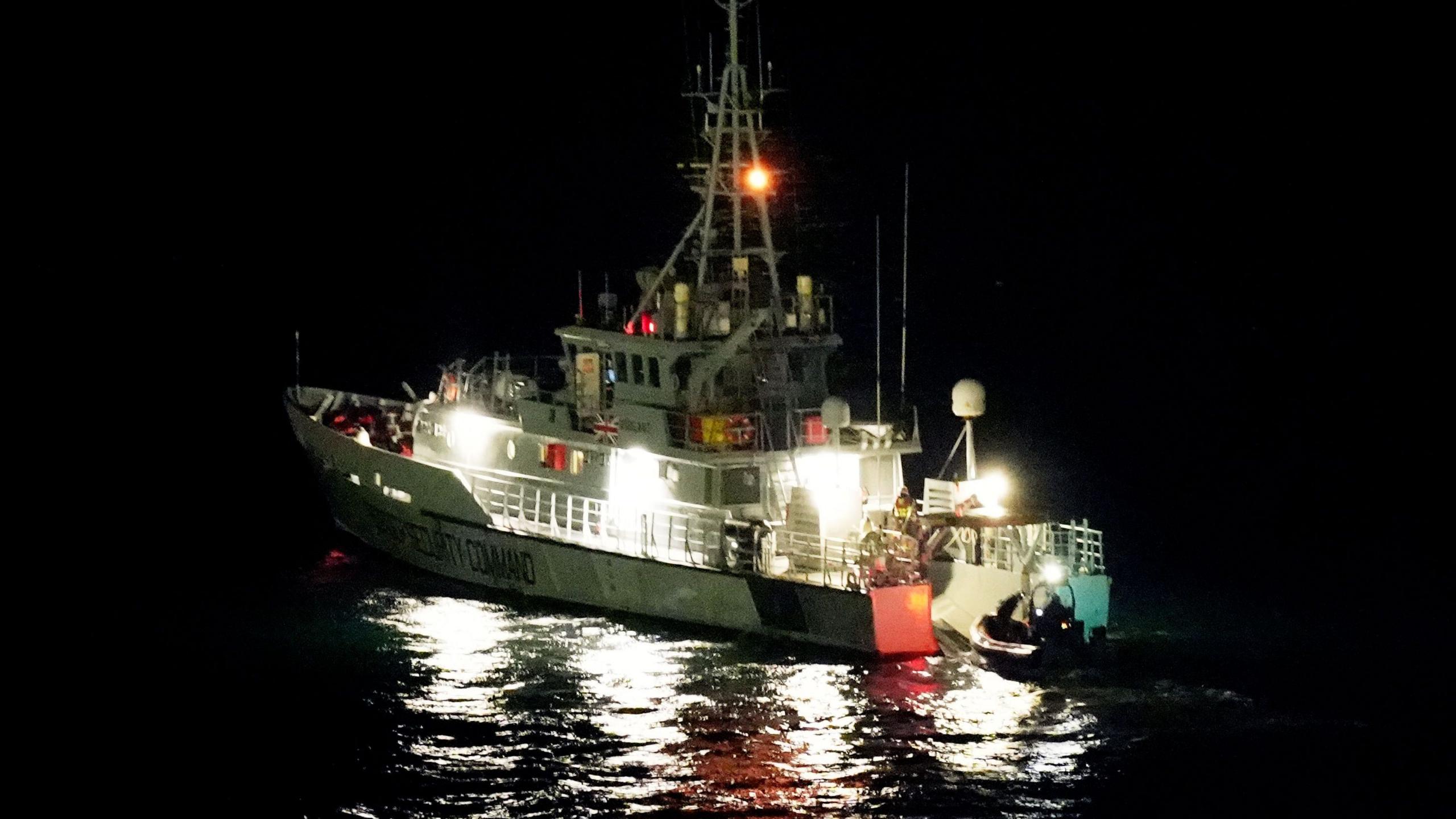 A boat in the pitch black. Bright lights shine from it, which reflect in the water.