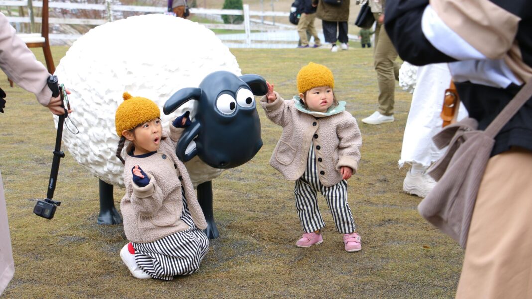 ‘Gromit was nearly a cat!’: Secrets from 50 years of Aardman Two small Asian children are posing with a Shaun the Sheep statue. They are wearing matching outfits with yellow hats, beige fleece jackets and matching stripey trousers.