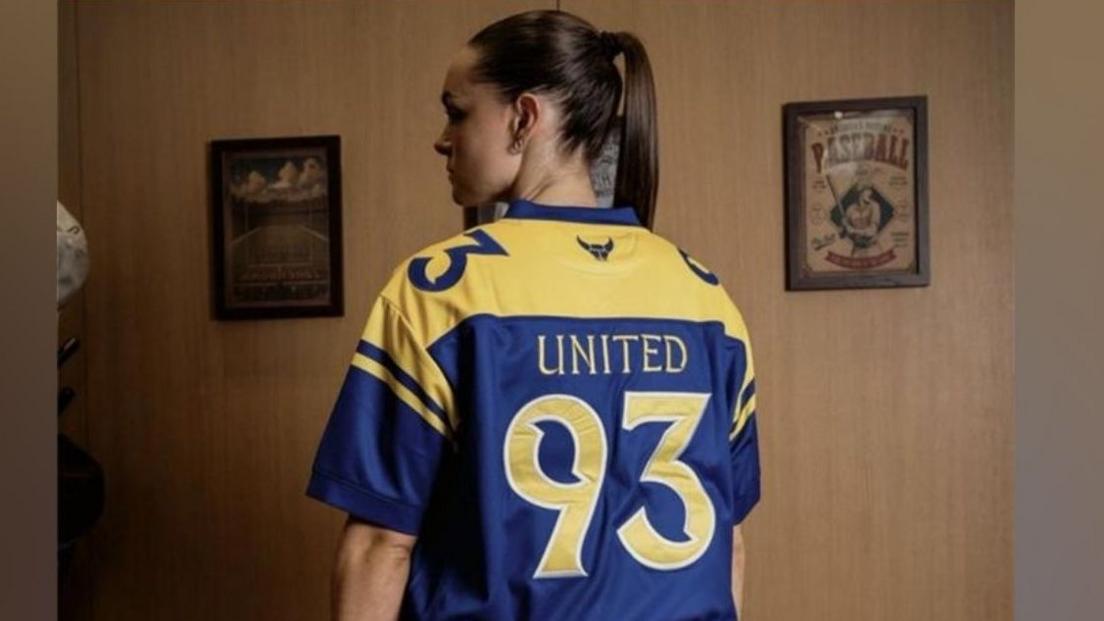 Female model wearing a yellow and blue shirt with "United 93" on the back