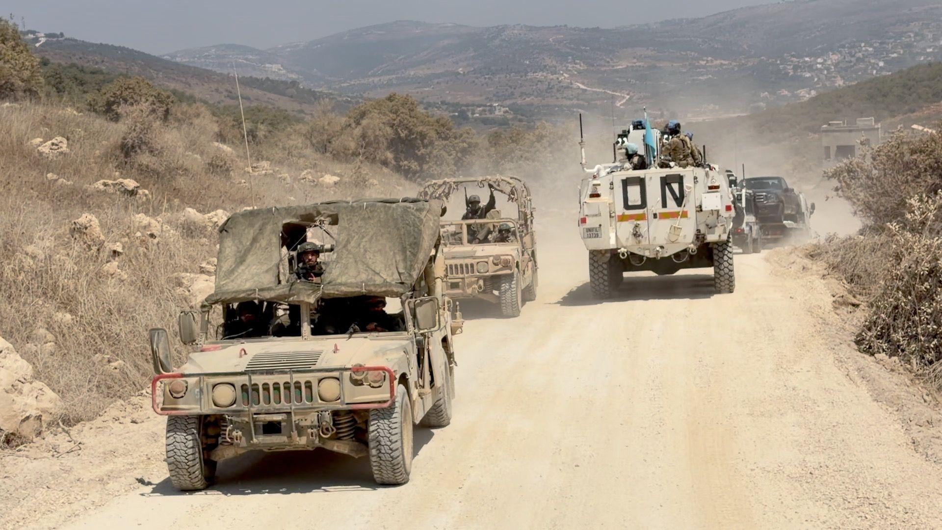 Two Israeli military vehicles pass a Unifil convoy on a road along the wall separating Lebanon and Israel
