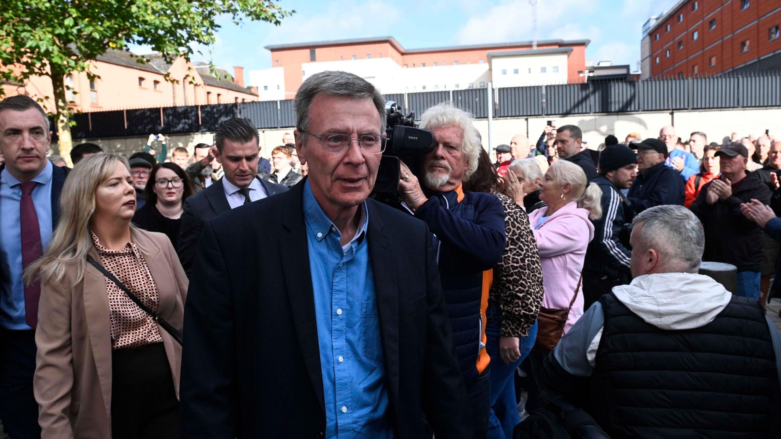 Breandan Mac Cionnaith has short dark hair and glasses and is walking among a crowd outside coiurt