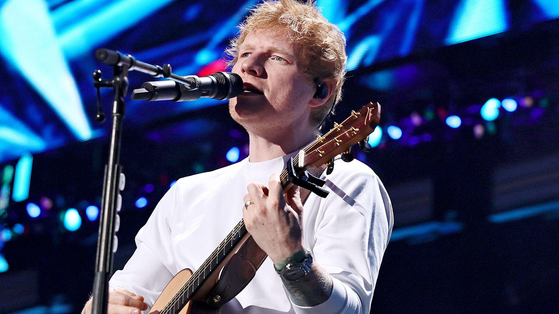 English singer songwriter in front of a microphone carrying his guitar onstage.
