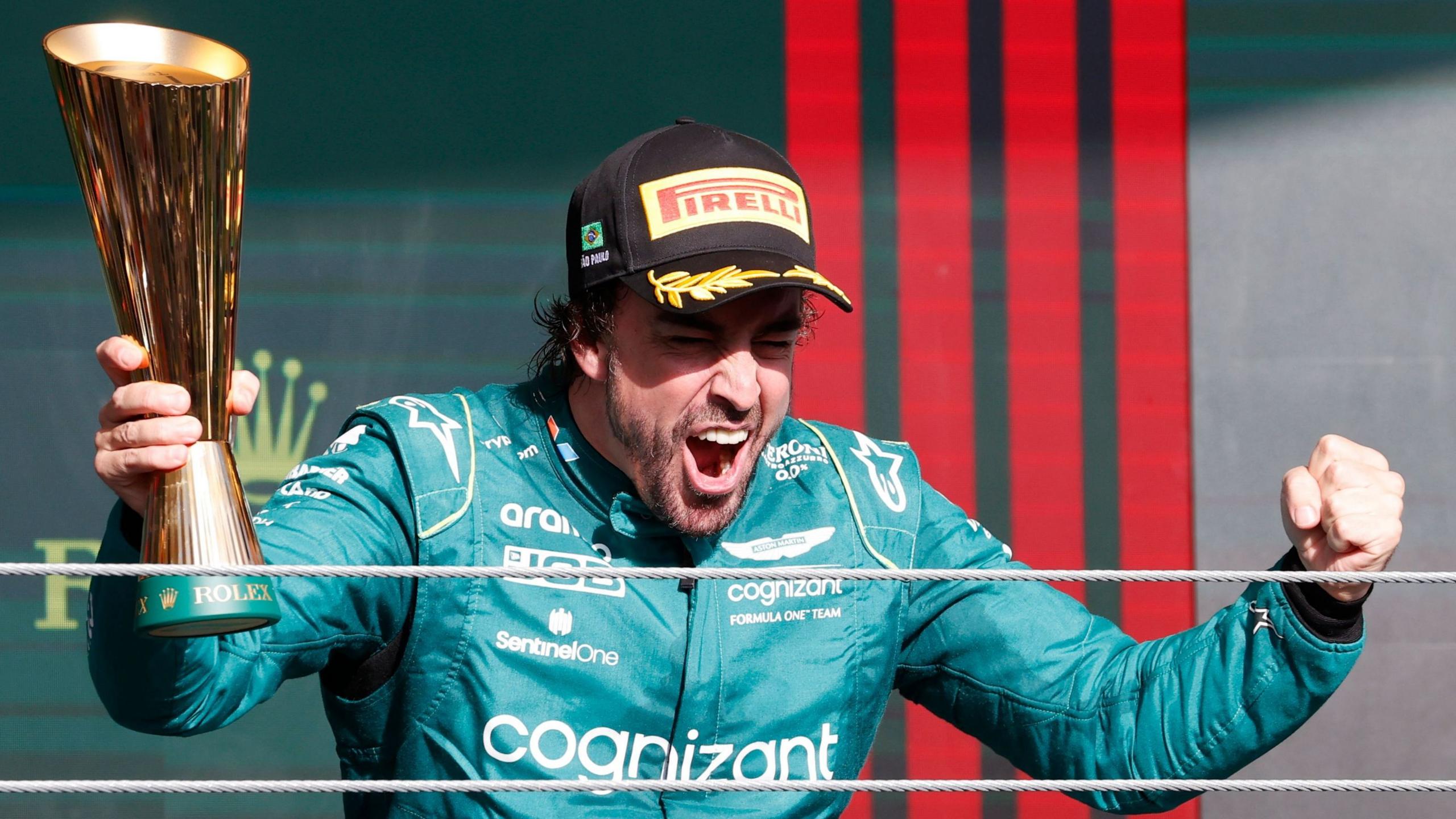 Fernando Alonso clenches his fists in celebration while holding a trophy after finishing third in the 2023 Sao Paulo Grand Prix